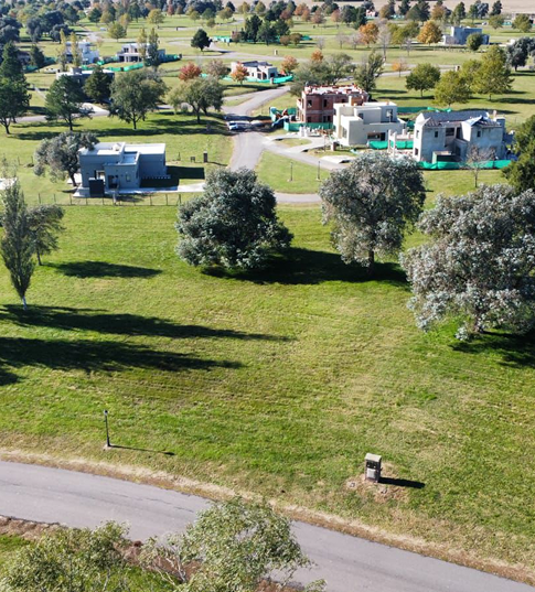 Vista aérea de un barrio en desarrollo con amplios espacios verdes, árboles dispersos, calles internas y viviendas modernas en construcción.
