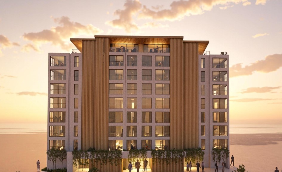 Render de un edificio moderno frente a la playa al atardecer, con el mar en primer plano y personas caminando por la orilla bajo un cielo naranja.