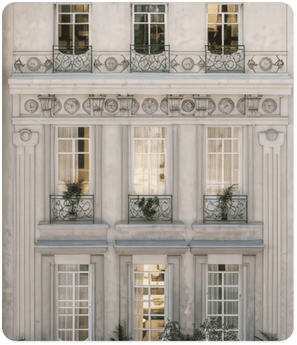 Fachada clásica de edificio con columnas, balcones de hierro forjado y ventanas altas de estilo europeo.