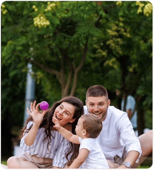 Familia jugando en un parque al aire libre, con padres sentados sobre el césped.