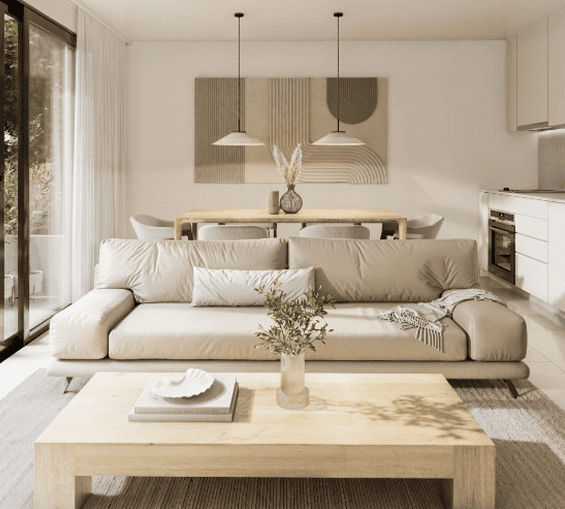 Living-comedor moderno y luminoso con sofá beige, mesa de madera, lámparas colgantes y cocina integrada al fondo.